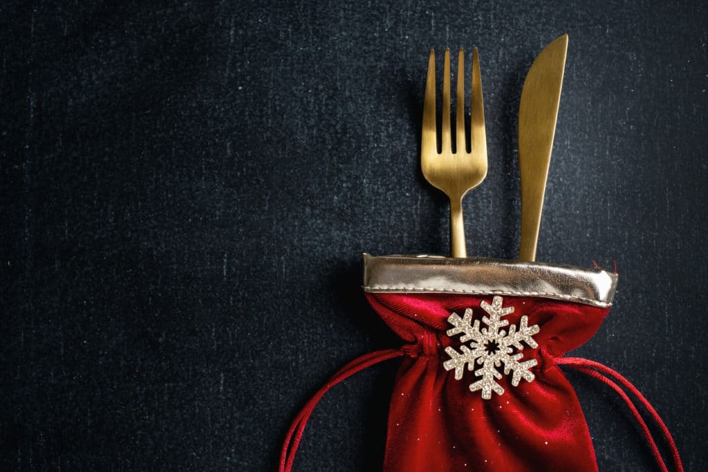 christmas golden cutlery in small textile bag with snowflake and ribbon on dark background