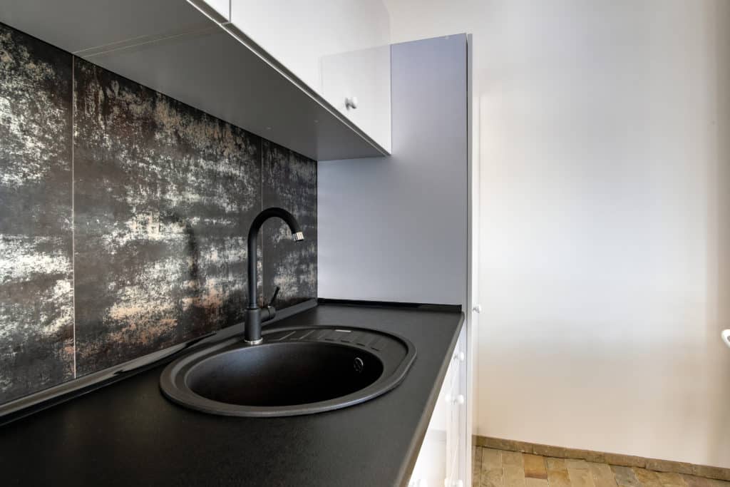 interior of modern spacious kitchen with white contemporary furniture black ceramic tiles on the wall and dark granite sink with water tap